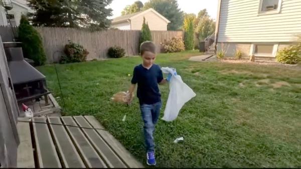 Boy holding a plastic bag searches a backyard for dog poop.